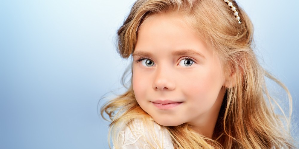 Portrait eines kleinen Mdchens mit langen blonden Haaren und Perlenschmuck im Haar, blauer Hintergrund