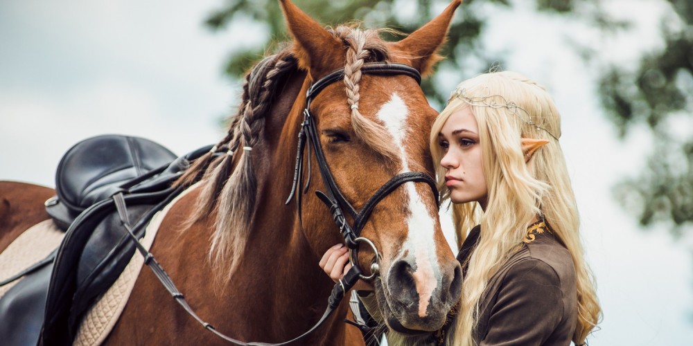 Blonde Elfenfrau mit spitzen Ohren steht an ihrem Pferd