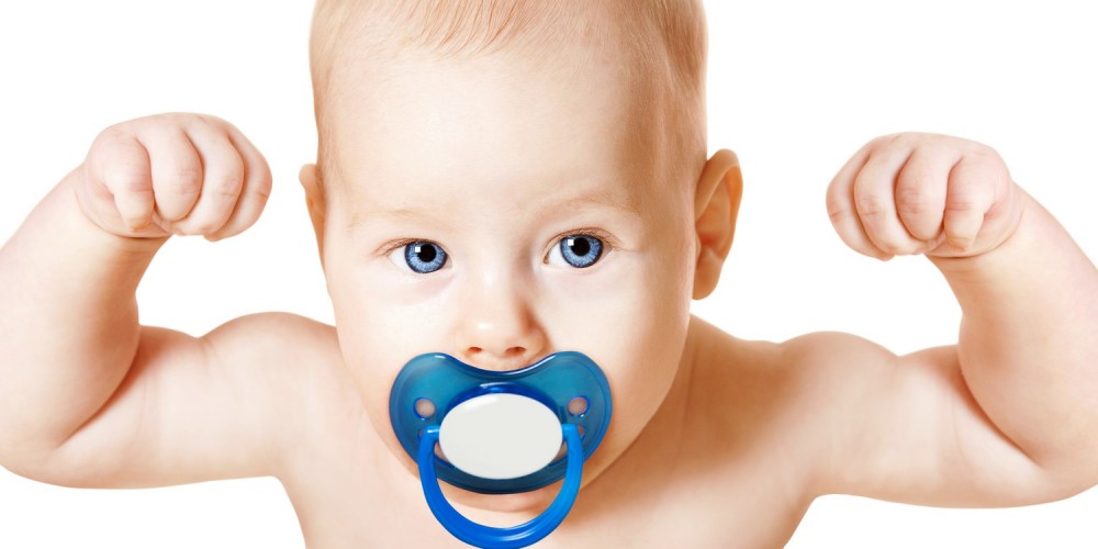 Blondes Baby mit großem blauen Schnuller im Mund hebt die Arme zur Bodybuilder-Pose an