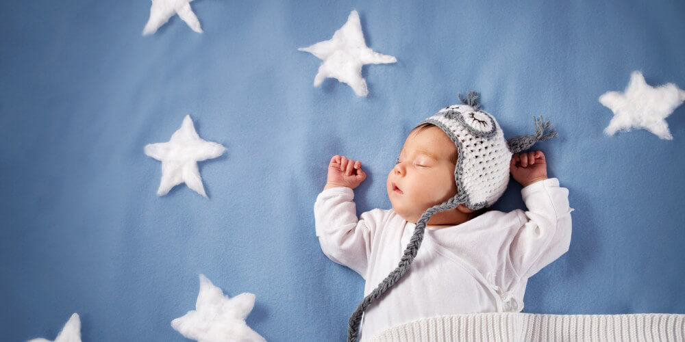 Baby mit Decke und Mtze schlft auf blauer Decke voller weier Sterne aus Watte