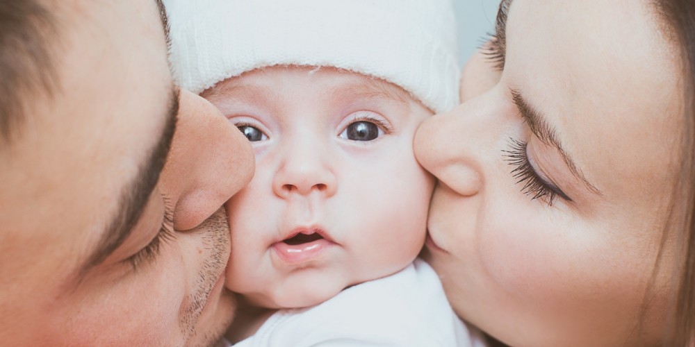 Sugling mit weier Wollmtze wird von Mama und Papa geksst