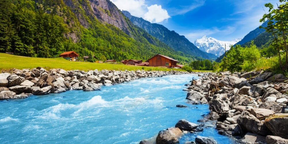 Flieender Bach/Fluss in einem schweizer Gebirge, im Hintergrund Huser und Berge