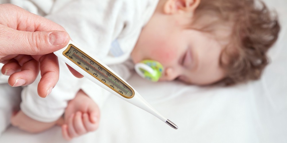 Schlafendes Kleinkind mit grnem Schnuller, im Vordergrund wird ein Fieberthermometer gehalten