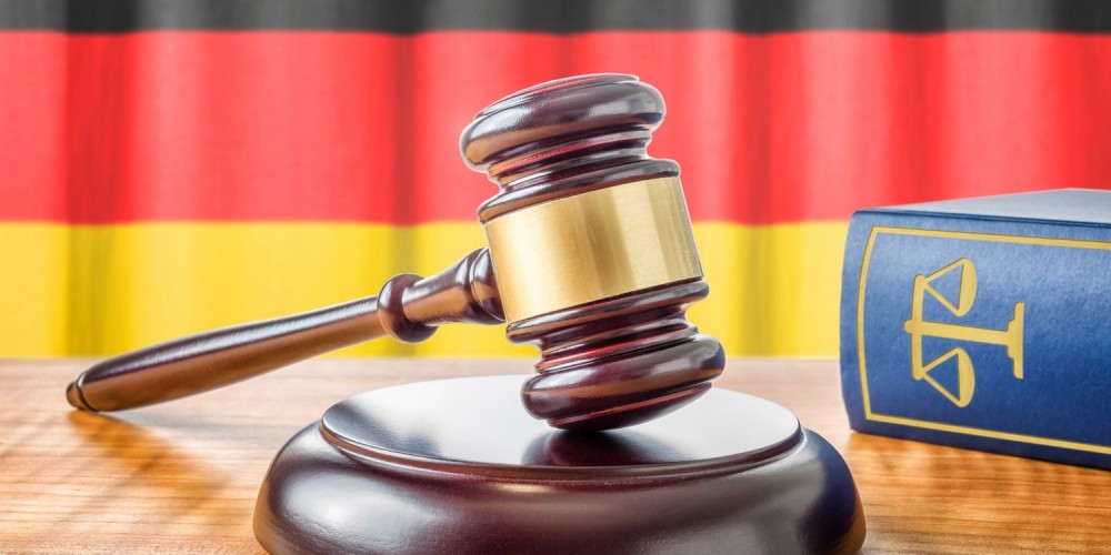 Richterhammer neben blauem Gesetzbuch vor Deutschlandflagge