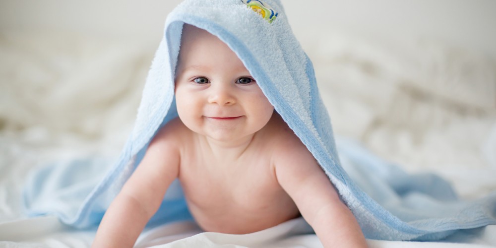 Glückliches Baby unter hellblauem Handtuch