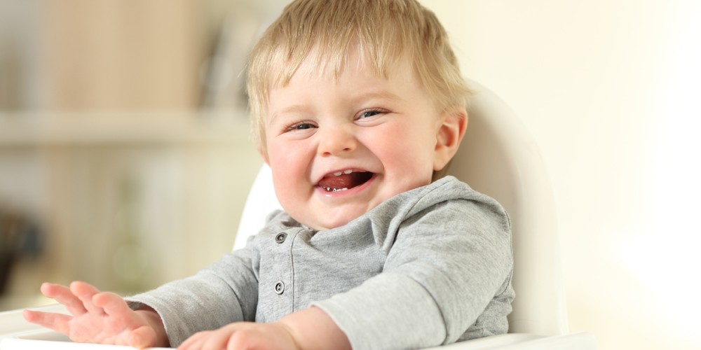 Lachender kleiner Junge sitzt im Hochstuhl