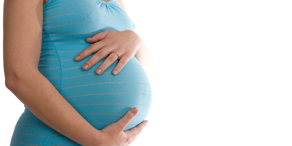 Schwangere Frau in blauem Top hlt sich den Bauch mit beiden Hnden