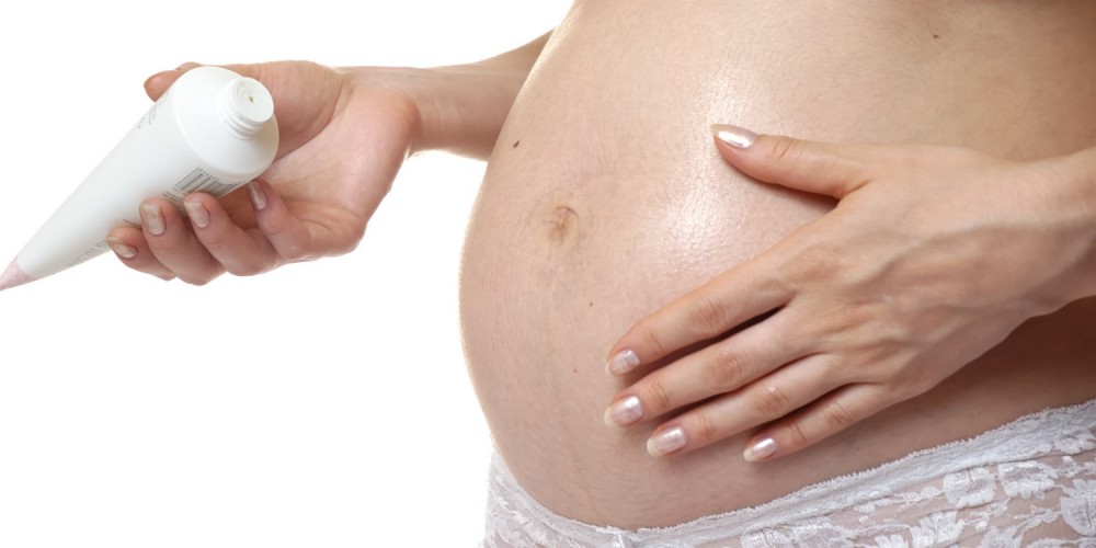 Schwangere Frau cremt ihren Bauch ein