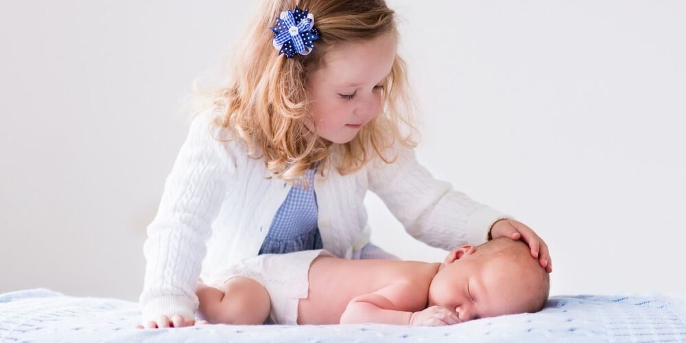 Kleines Mädchen streichelt ihr neugeborenes Geschwisterchen
