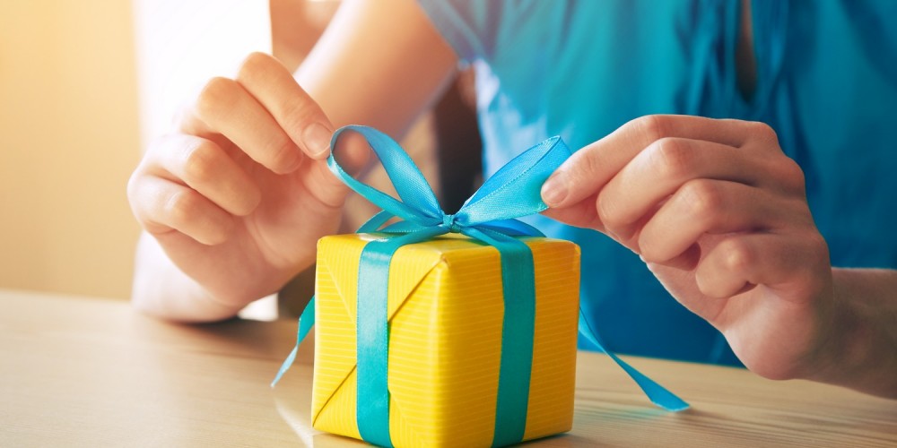 Frau bindet eine blaue Schleife an eine kleine gelbe Geschenkbox