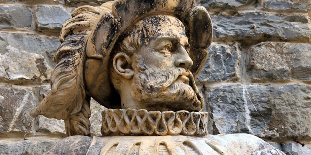 Alte grau-braune Marmorstatue eines Edelmannes vor einer alten Steinmauer