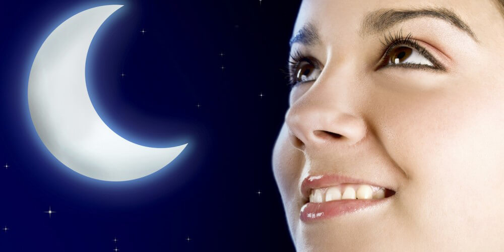 Junge Frau schaut lächelnd in den Himmel, im Hintergrund Grafik Halbmond und Sterne