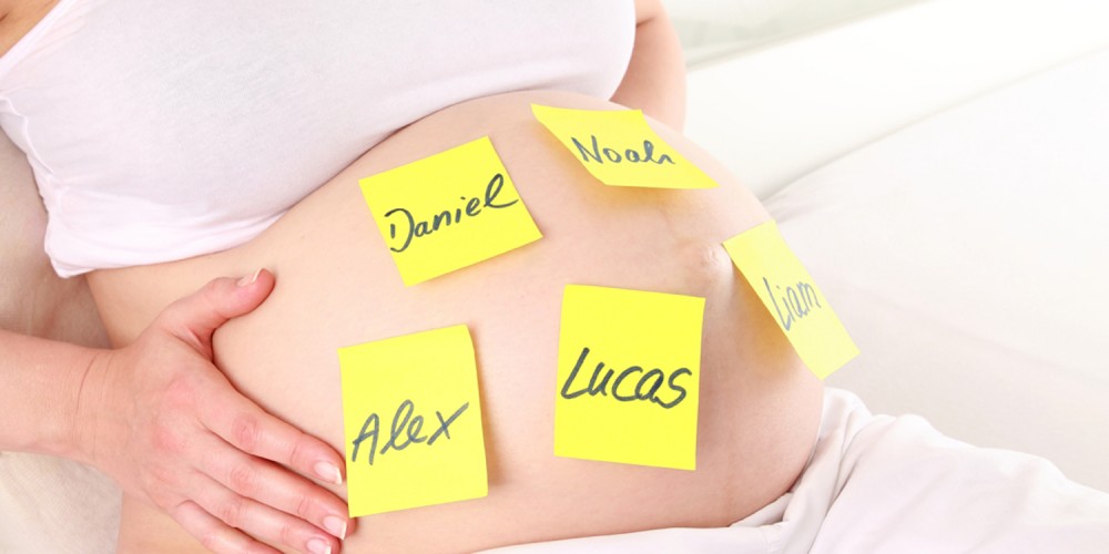 Schwangere Frau mit fünf gelben Post-its auf dem Babybauch, auf denen Jungennamen geschrieben sind