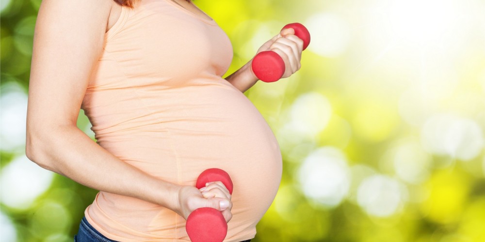 Schwangere Frau mit zwei kleinen roten Kurzhanteln im Grnen