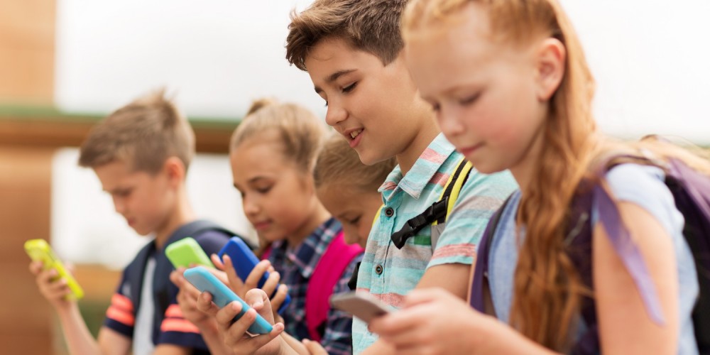Fünf junge Schüler mit Schulrucksack befassen sich alle mit ihrem Smartphone