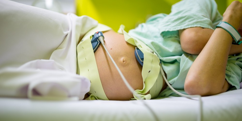 Schwangere Frau liegt im Krankenhausbett auf der Seite und ist am Wehenschreiber (CTG) angeschlossen